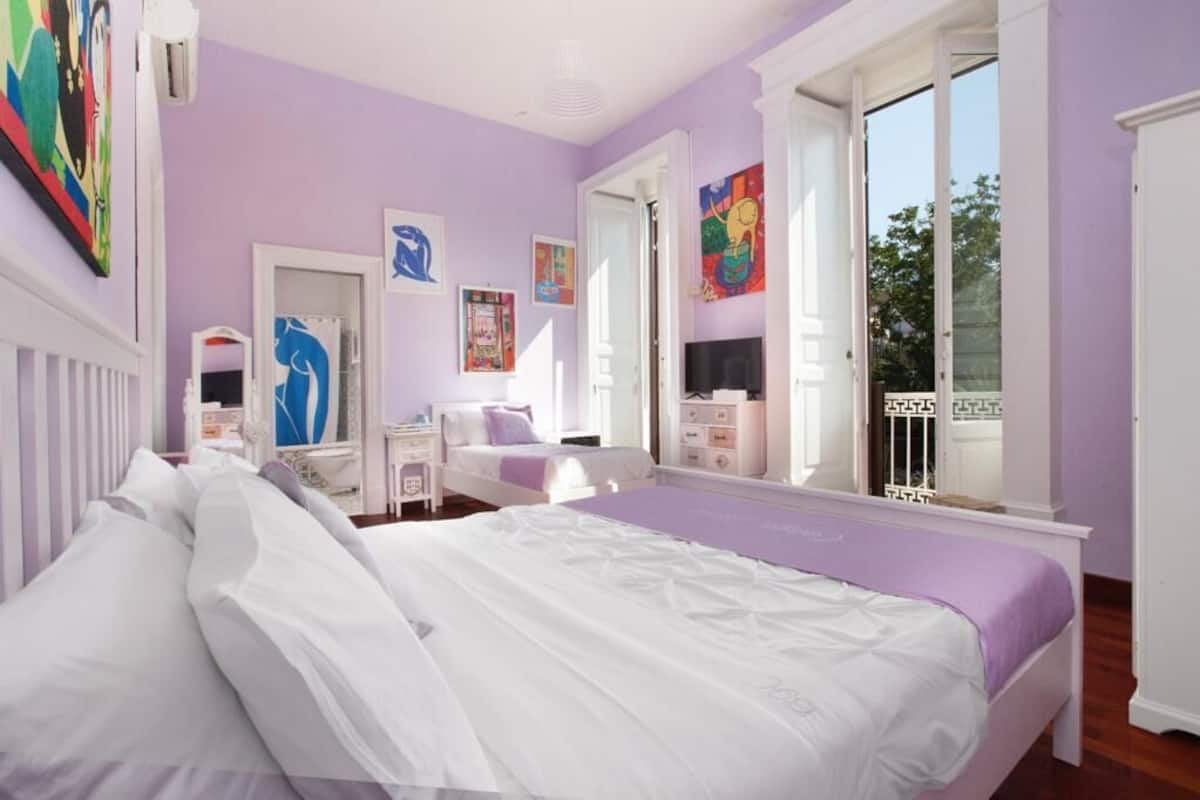 A bedroom with a large bed, a dresser, a vanity, and a window with a view of the outdoors.