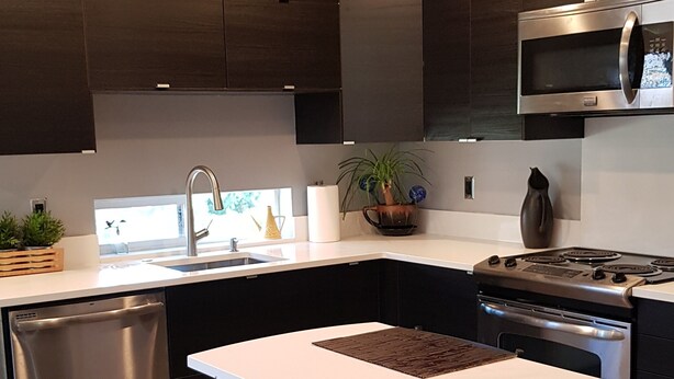 A modern kitchen with dark cabinetry, stainless steel appliances, a white countertop, and a dining area with two chairs. - Modern condo near Microsoft for business and leisure travelers (Bellevue)