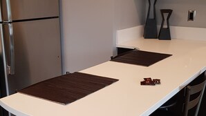 A kitchen with a white countertop, two black stools, and a stainless steel refrigerator. - Modern condo near Microsoft for business and leisure travelers (Bellevue)