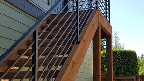 A wooden staircase leading to a balcony with a metal railing, attached to a house with light green siding. - Modern condo near Microsoft for business and leisure travelers (Bellevue)