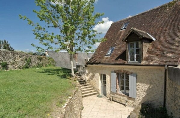 A stone house with a sloped roof, a small porch, and a staircase leading to the entrance.