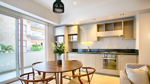 A modern kitchen with built-in appliances, a dining area with a round table and chairs, and a balcony with a view of greenery. - Romantic Zone Gem | 2 Pools, Gym | Walk to Beach (Puerto Vallarta)