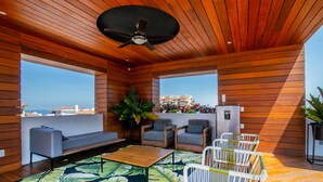 A modern outdoor living area with wooden paneling, a ceiling fan, a sofa, two armchairs, a coffee table, and a patterned rug. - Romantic Zone Gem | 2 Pools, Gym | Walk to Beach (Puerto Vallarta)