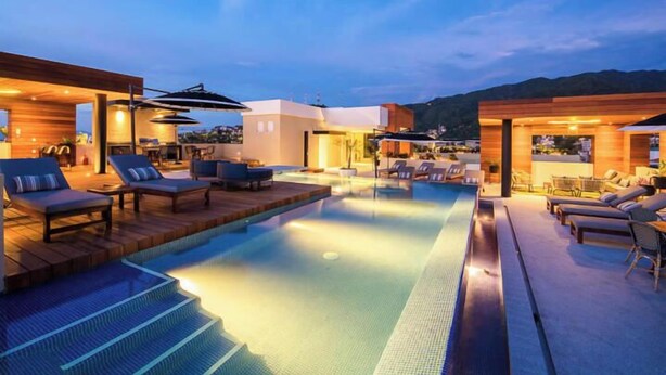 A rooftop infinity pool with lounge chairs and umbrellas, surrounded by modern architecture and a view of the mountains. - Romantic Zone Gem | 2 Pools, Gym | Walk to Beach (Puerto Vallarta)