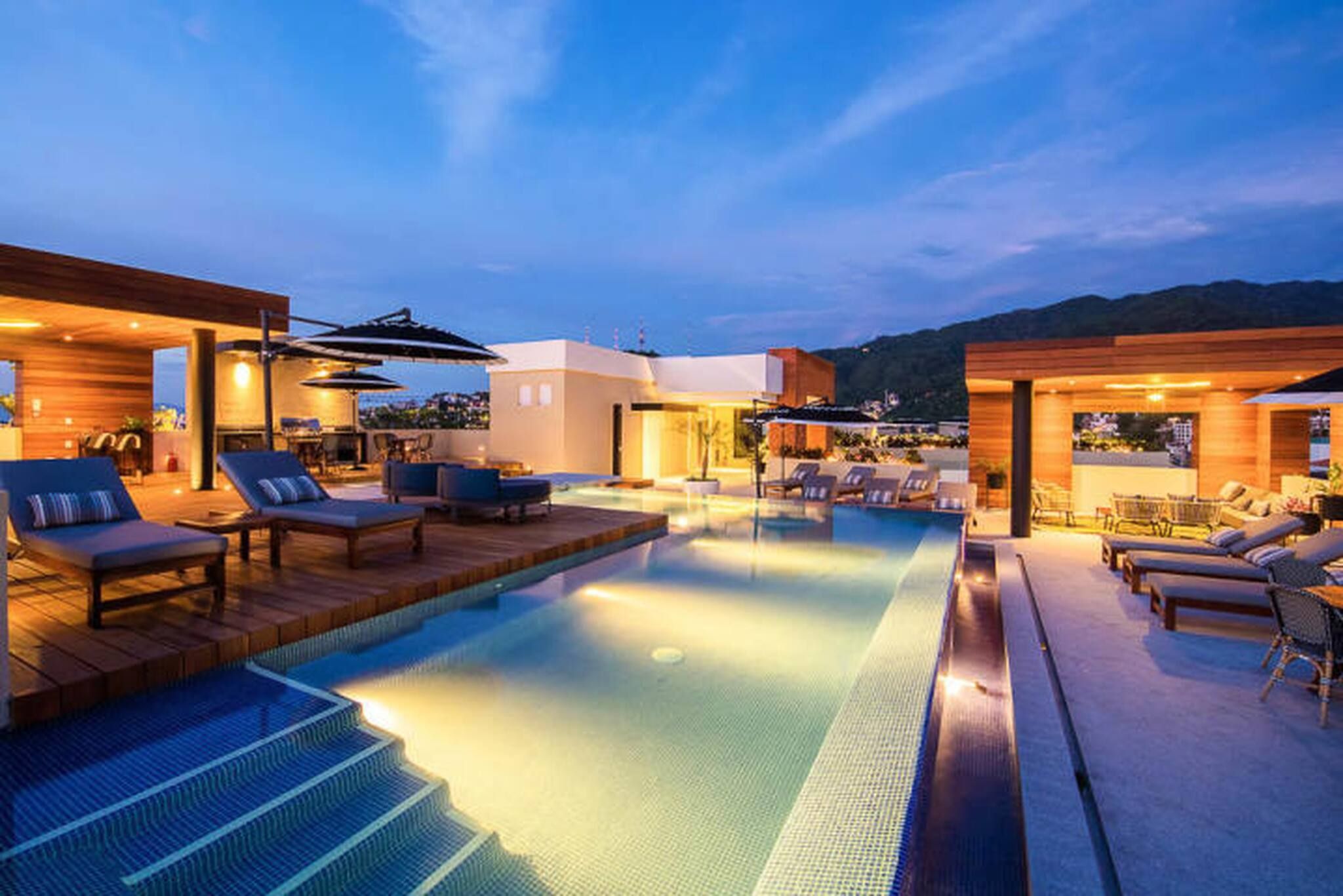 A rooftop pool area with lounge chairs and umbrellas, surrounded by modern buildings.