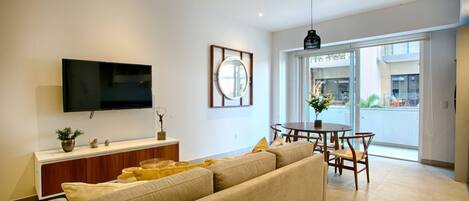 En moderne stue med et fladskærms-tv, et rundt spejl, en sofa, et spisebord med stole og en balkon med udsigt.