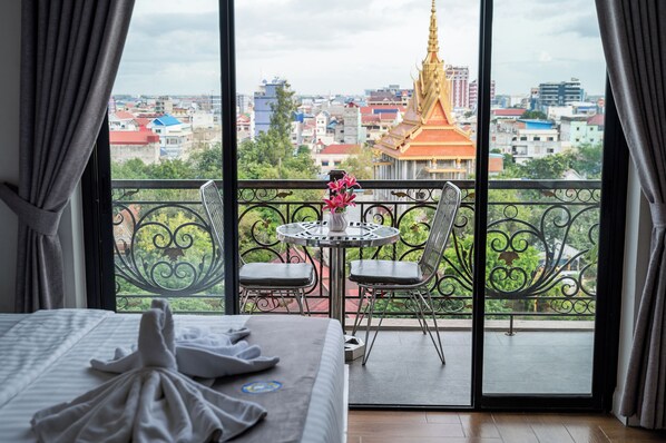 A hotel room with a balcony, a bed, a table with chairs, and a vase with flowers. - Hak Huot Hotel (Ou Chrov)