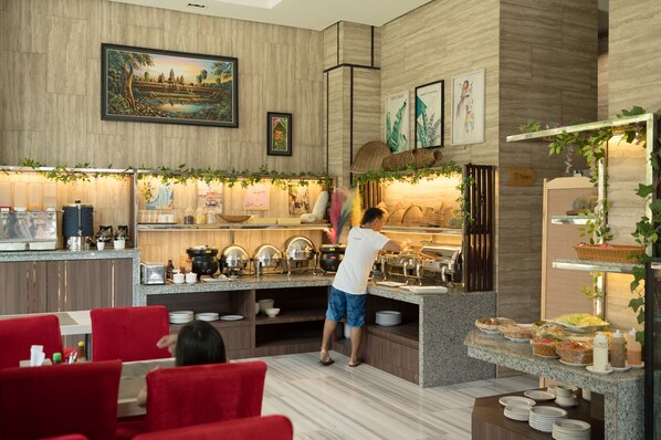 A modern kitchen with granite countertops, a buffet setup, and a dining area with red chairs. - Hak Huot Hotel (Ou Chrov)