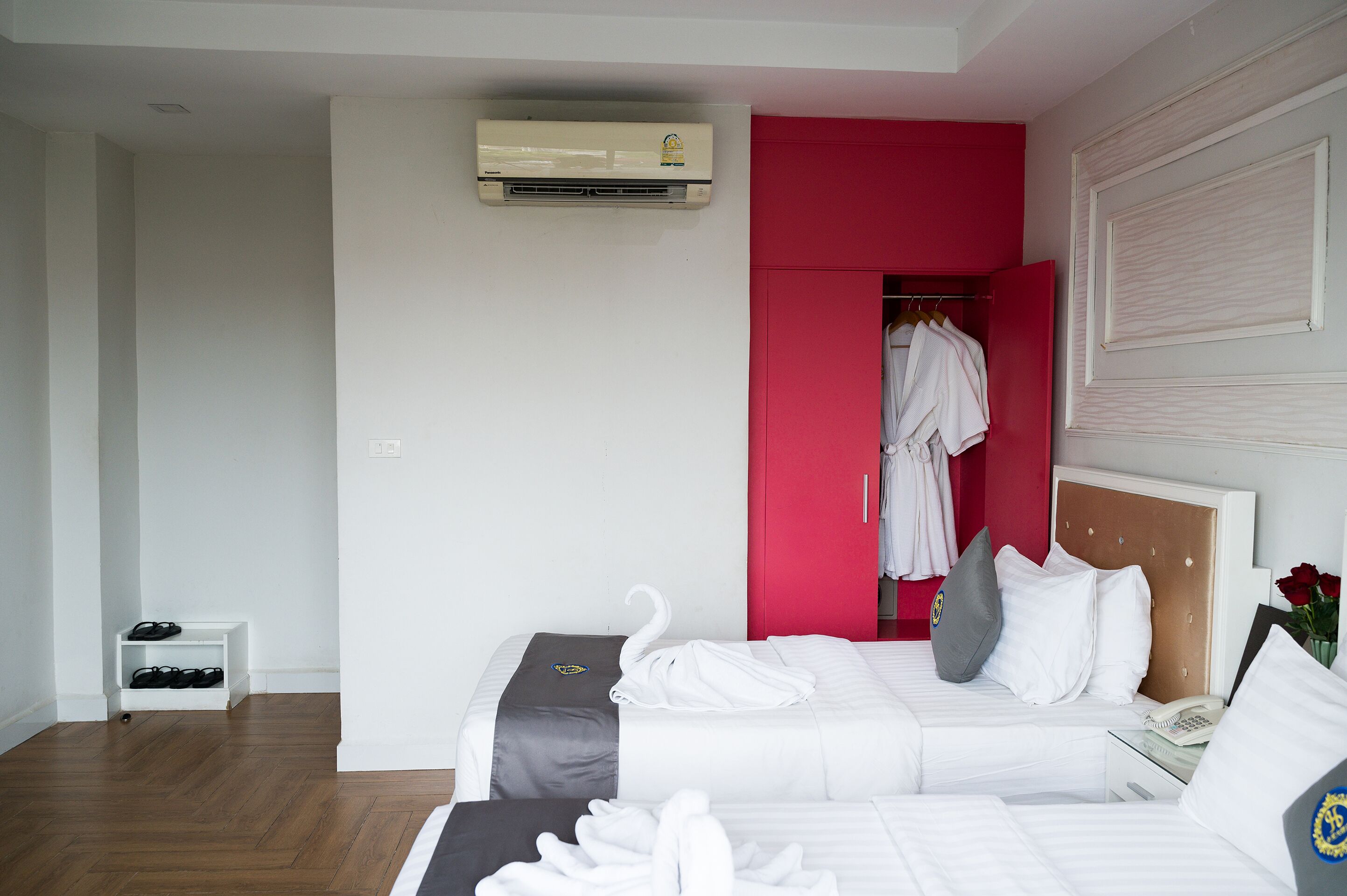A hotel room with a bed, a bedside table with a phone, a shoe rack, and a red wardrobe.