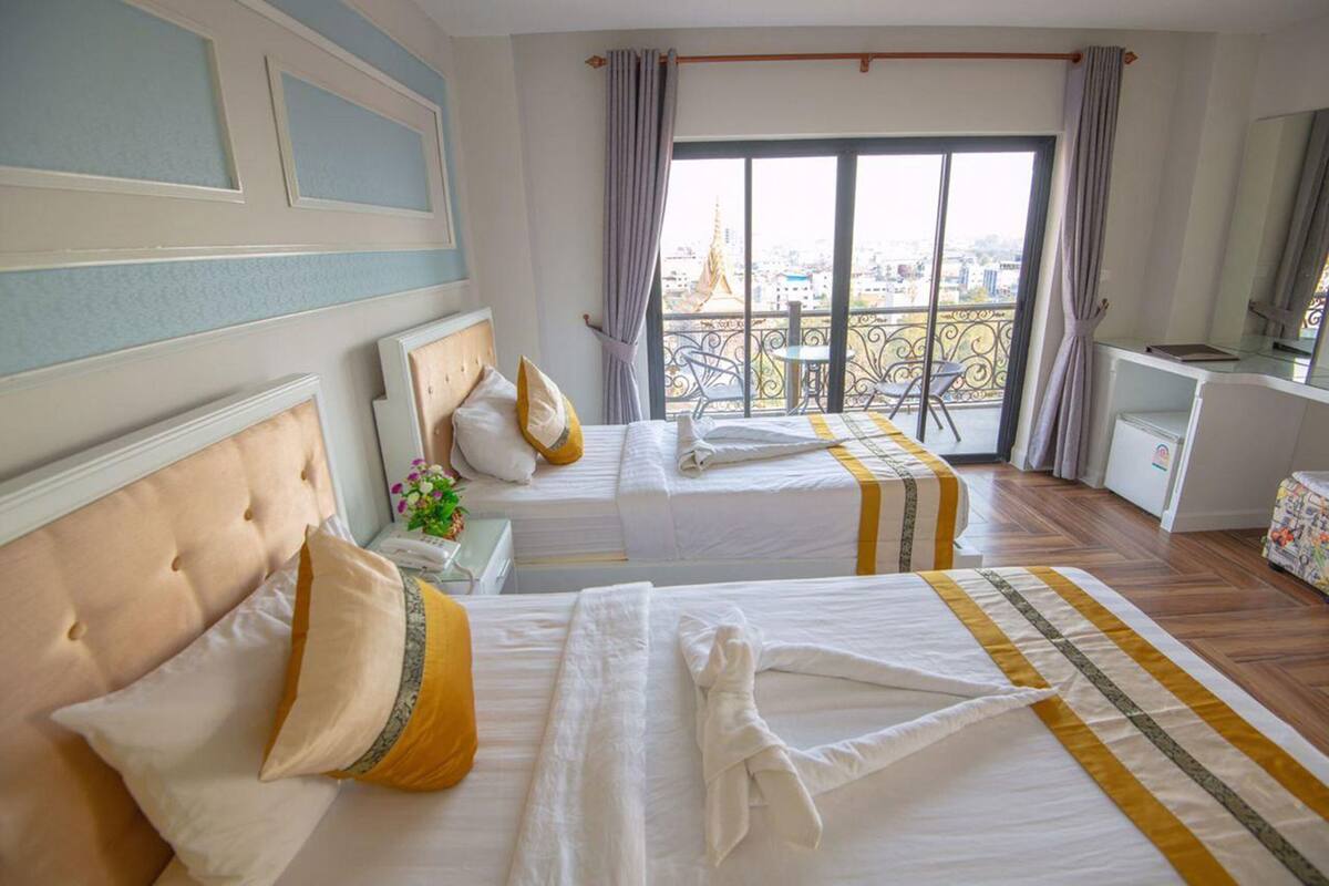 Ein Hotelzimmer mit zwei Betten, einem Balkon mit Blick, einem kleinen Schreibtisch und einem fenster mit Vorhängen.