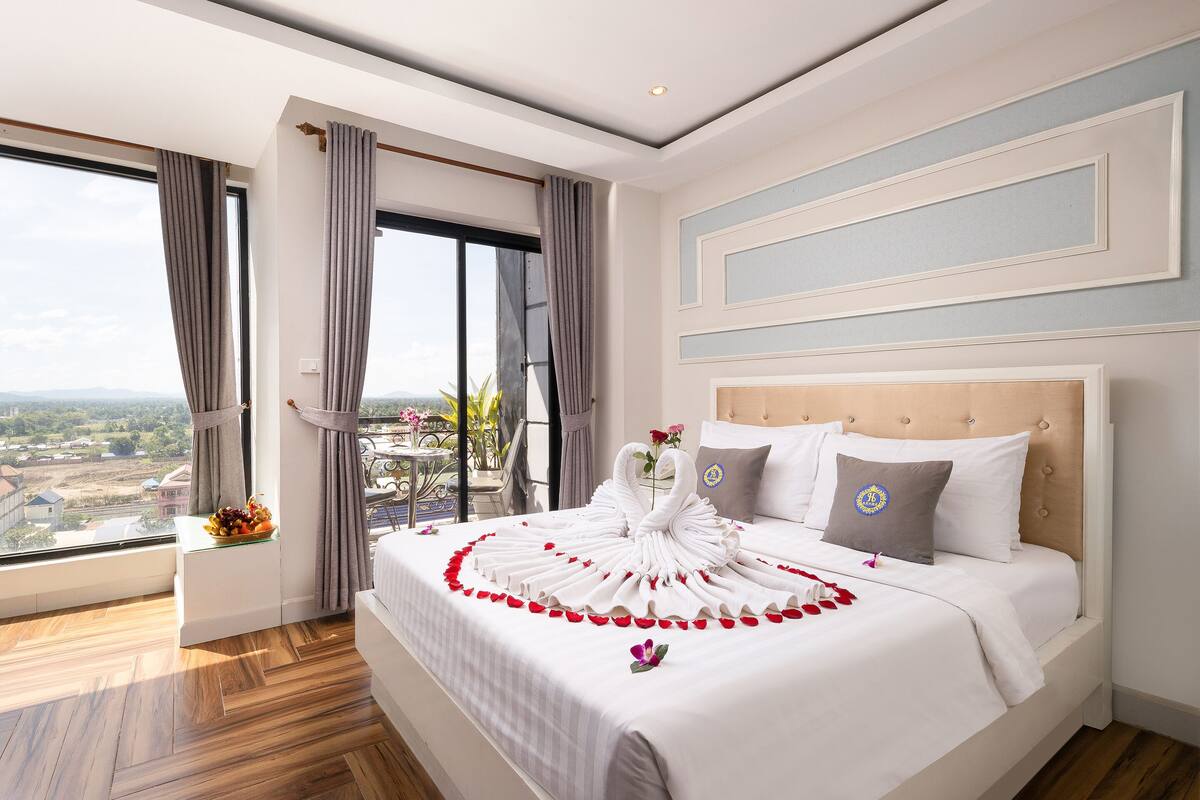 Ein Hotelzimmer mit großem Bett, Blick auf die Stadt und einem Balkon mit Tisch und Stühlen.