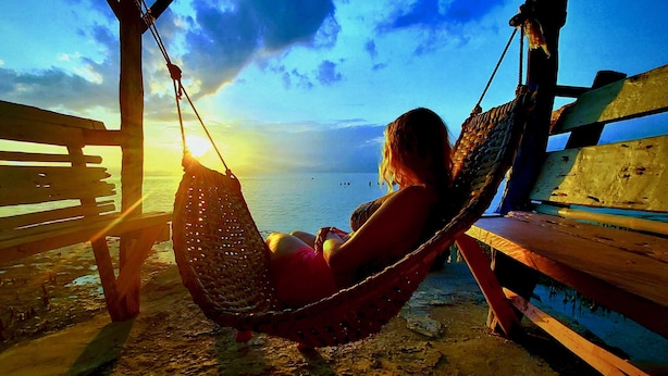 Una persona relajándose en una hamaca con vista al mar y al atardecer.