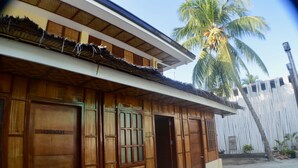 Una casa de madera tradicional con techo de paja y una palmera al fondo.