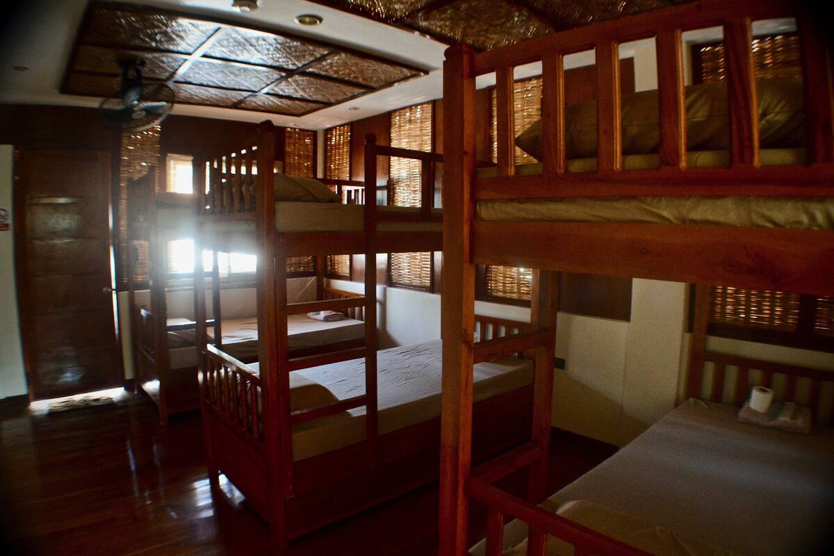 A room with wooden bunk beds, a ceiling fan, and a view of the outside through large windows.