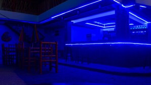 Una habitación con zona de bar, iluminación azul tenue, mobiliario de madera y suelo de piedra.