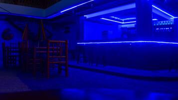 A room with a bar area featuring blue ambient lighting, wooden furniture, and a stone floor.