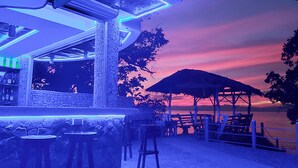 Zona de bar con pared de piedra, taburetes y vista al atardecer sobre el agua.