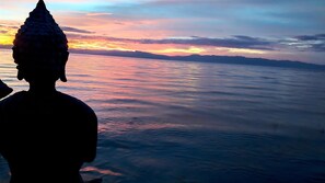 Una estatua domina una masa de agua, con un atardecer de fondo.
