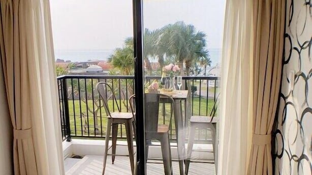 A hotel room with a bed, a balcony with a table and chairs, and a view of the outdoors.