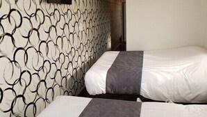 A hotel room with two beds, a patterned wall, and a flat-screen TV mounted on the wall.