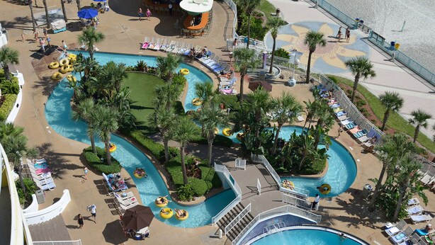 Zona de piscina en un resort con toboganes acuáticos, sillas de descanso y palmeras.