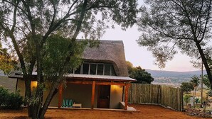 A rustic house with a thatched roof, surrounded by trees and a wooden fence. - Rocky Hollow Guest Farm (Pretoria)