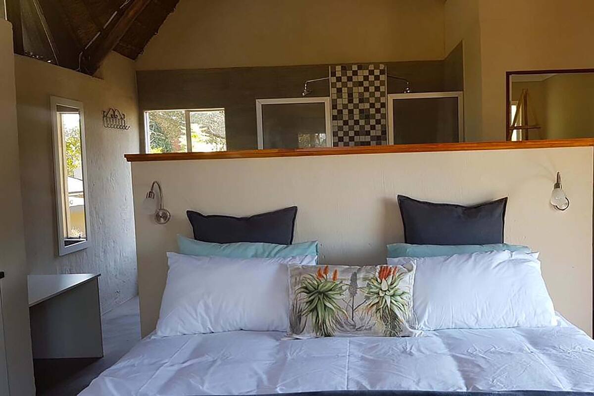 A bedroom with a bed, two pillows, a decorative pillow, a window, and a mirror.