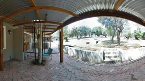 A covered outdoor area with a brick floor, wooden beams, and a glass door leading to an interior space. - Rocky Hollow Guest Farm (Pretoria)