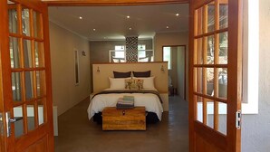 A bedroom with a large bed, a wooden chest of drawers, and a view of the bathroom through an open door. - Rocky Hollow Guest Farm (Pretoria)