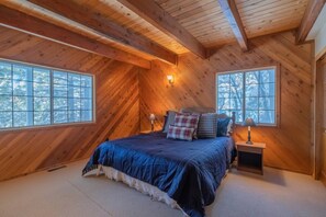 Un dormitorio con una cama grande, dos mesitas de noche y una ventana con vista a árboles.