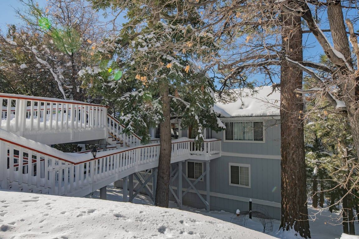 Un edificio de varios pisos con una escalera blanca que conduce a un balcón, rodeado de árboles cubiertos de nieve.