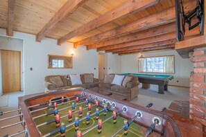 Ein Raum mit einer Fußballtischkickeranlage, zwei Sofas, einem Billardtisch und einer Ziegelwand.