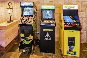 Three arcade machines, including Pac-Man, in a room with a wooden cabinet and a wall-mounted lamp.