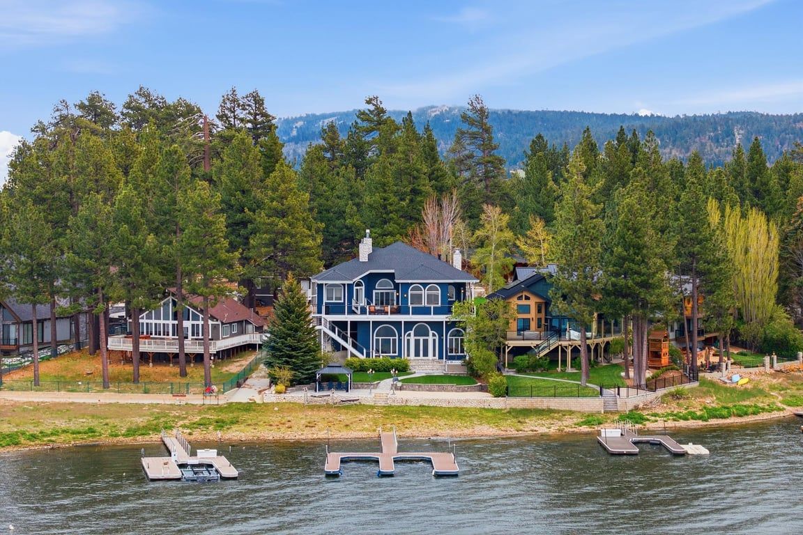 Een pand aan het water met een groot huis, een aanlegsteiger en omliggend bos.