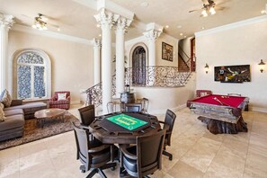 Une pièce spacieuse équipée d’une table de billard, d’une table de jeu de flipper et d’un coin salon avec un canapé et des fauteuils.