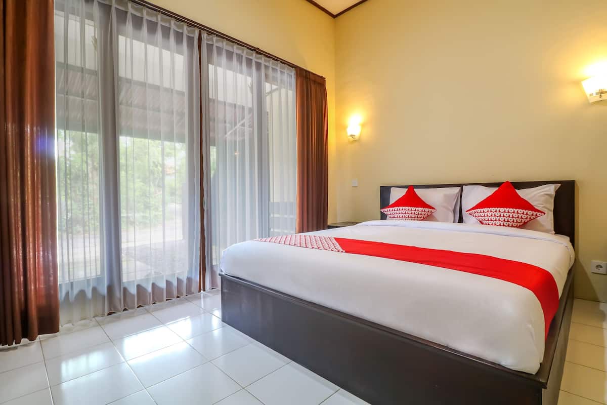 A hotel room with a large bed, a sliding glass door, and a wall-mounted light fixture.