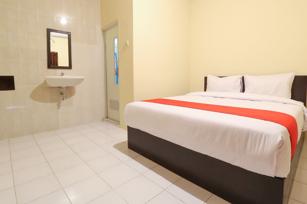 A hotel room with a bed, a bedside table, a mirror, and a bathroom with a sink and shower.