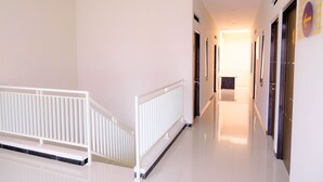 Un pasillo limpio y bien iluminado con barandilla blanca, puertas y un reloj en la pared.