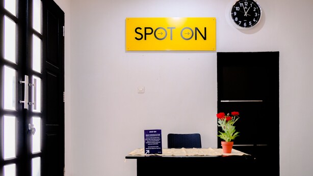 Zona de recepción con un letrero 'SPOT ON', un reloj, un escritorio con una planta en maceta y una silla.