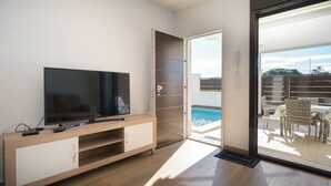 A modern living room with a flat-screen TV, wooden entertainment unit, and a sliding glass door leading to a poolside area. - Villa Stachera (San Pedro del Pinatar) (San Pedro del Pinatar)