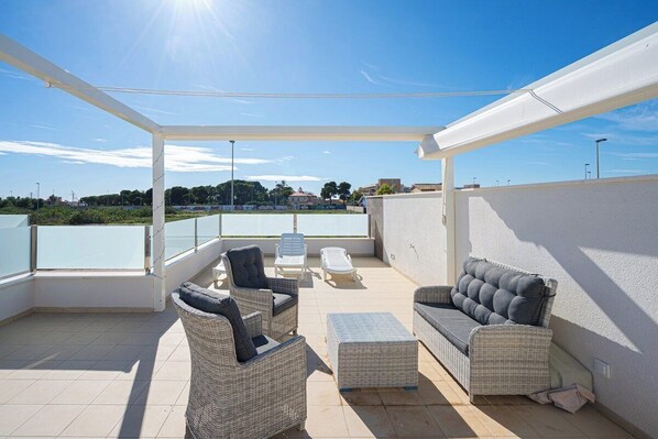 A covered outdoor patio with wicker furniture, a view of the city, and a clear sky.