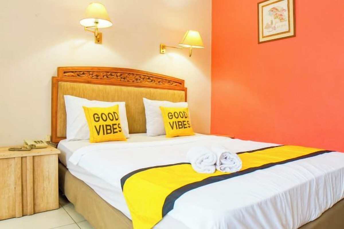 A hotel room with a bed, two bedside lamps, a nightstand, and a wall with a framed picture.