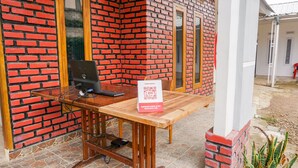 A check-in station with a laptop, a QR code sign, and a brick wall. - OYO 2369 Cempaka Homestay (Rancabali)