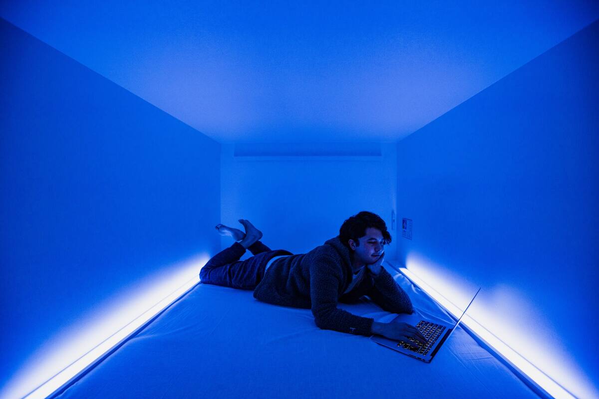 Une personne allongée sur un lit dans une pièce éclairée d’une lumière bleue.