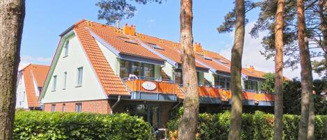 Un edificio moderno con techo inclinado, ventanas grandes y un balcón con barandillas naranjas.