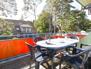 Eine Terrasse mit rundem Tisch und Stühlen, einem Sonnenschirm und Blick auf Bäume und Gebäude im Hintergrund.