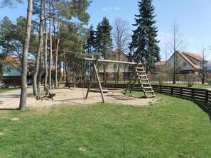 A playground with wooden swings and a climbing structure, surrounded by trees and a fenced area. - Papillon Whg. 11/7, Germany (Ostseebad Boltenhagen)