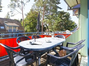Un balcon avec une table et des chaises, donnant sur un quartier résidentiel bordé d’arbres et de maisons.