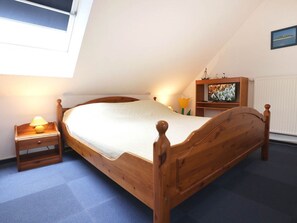 A bedroom with a wooden bed, a nightstand with a lamp, a shelf with decorative items, and a window providing natural light. - Papillon Whg. 11/7, Germany (Ostseebad Boltenhagen)