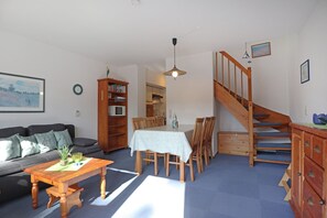 Un salon comprenant un canapé, une table basse, une table à manger avec des chaises, une bibliothèque, un escalier et un coin cuisine.